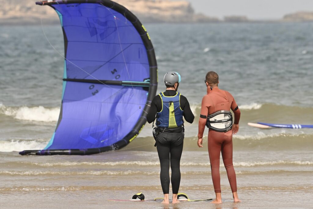 Élève et moniteur observant un kite bleu au bord de l’eau cours de wingfoil | élève et moniteur observant un kite bleu au bord de l’eau | 4